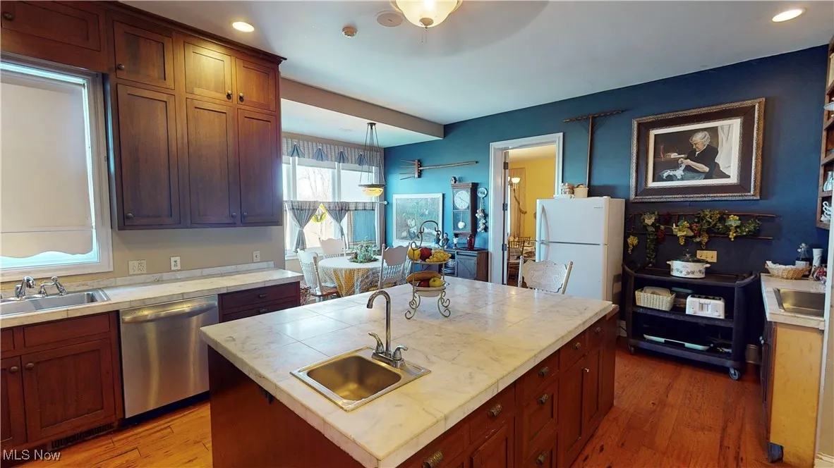 Kitchen with dishwasher, white refrigerator, dark hardwood / wood-style flooring, sink, and a kitchen island with sink