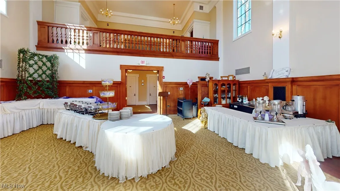Living room featuring crown molding, a towering ceiling, wooden walls, and a notable chandelier