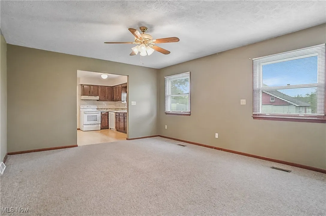Unfurnished living room with light colored carpet, a ceiling fan, and baseboards