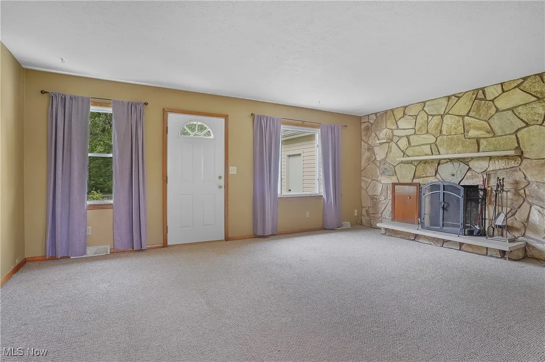 Unfurnished living room with a stone fireplace, carpet floors, and baseboards