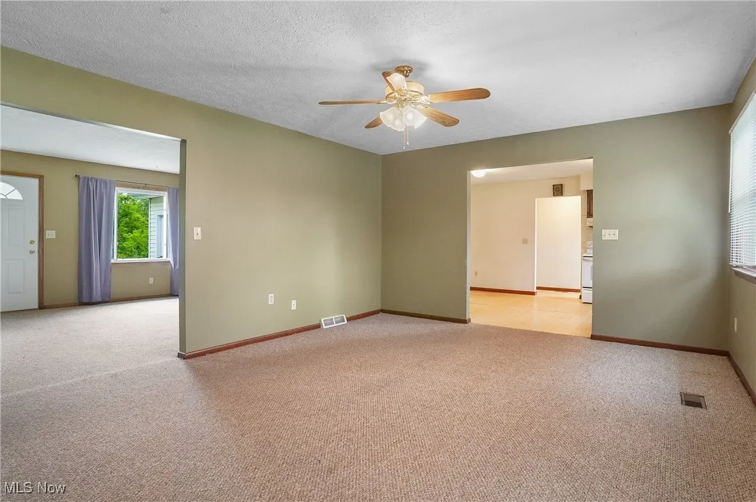 Unfurnished room with light carpet, a ceiling fan, and baseboards