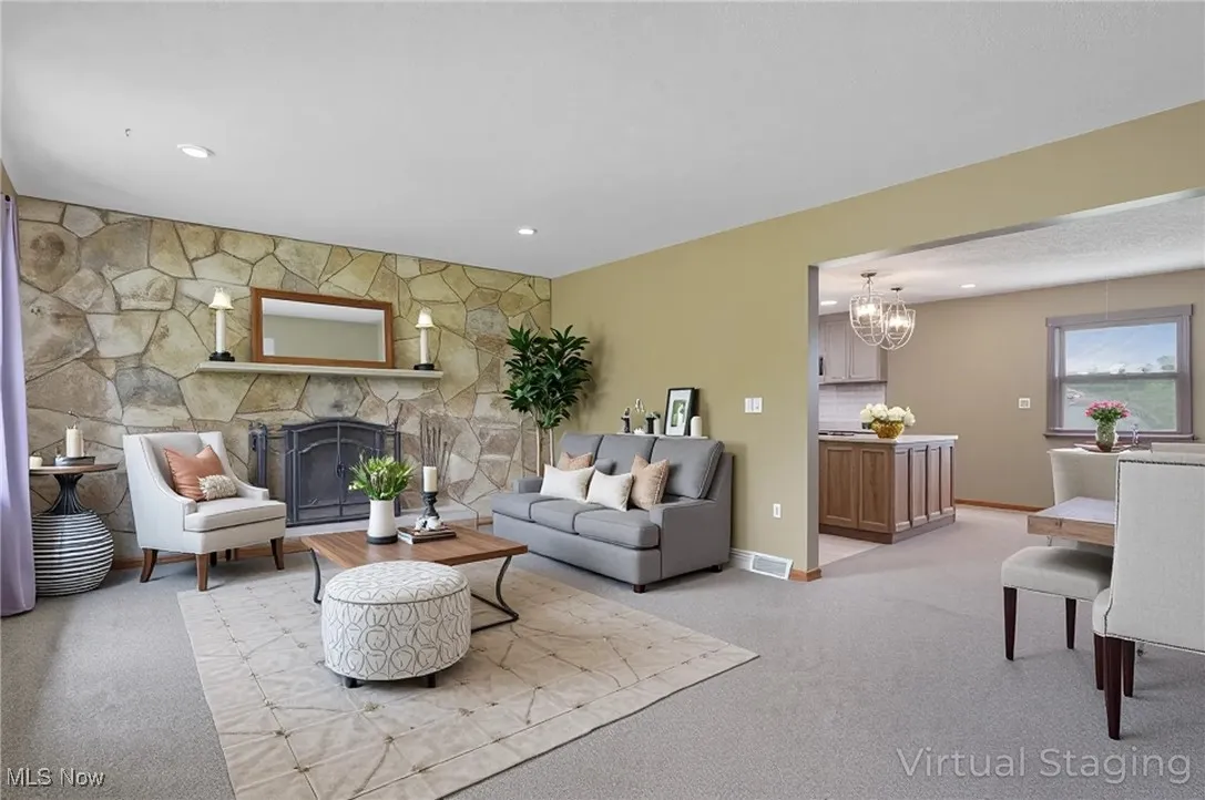 Living room with a chandelier, light carpet, a stone fireplace, baseboards, and recessed lighting