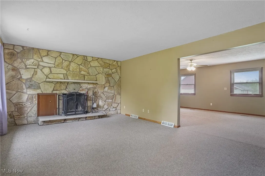 Unfurnished living room with carpet, a fireplace, ceiling fan, and baseboards