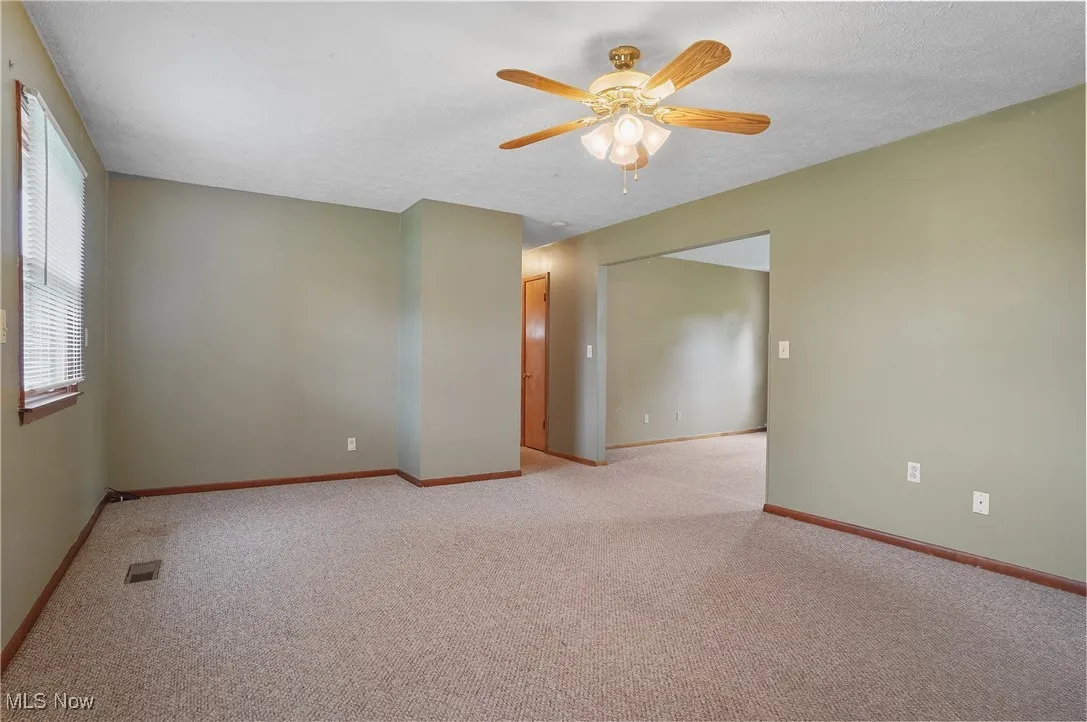 Unfurnished room featuring ceiling fan, light carpet, baseboards, and a textured ceiling