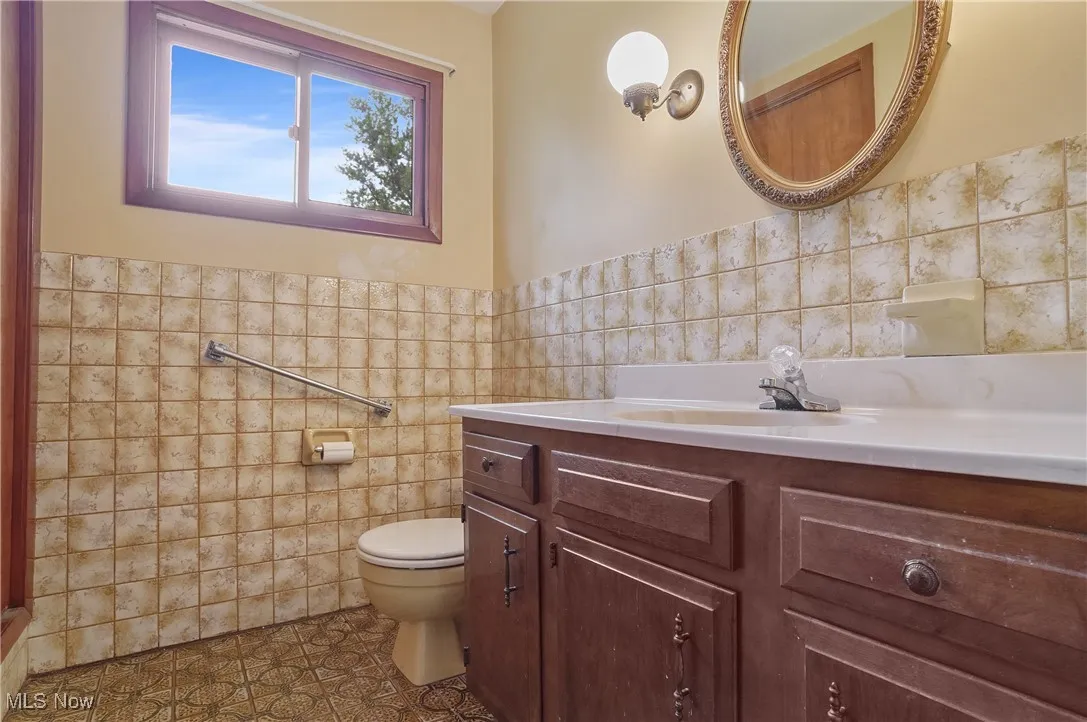 Bathroom with tile walls, toilet, vanity, tile patterned floors, and wainscoting