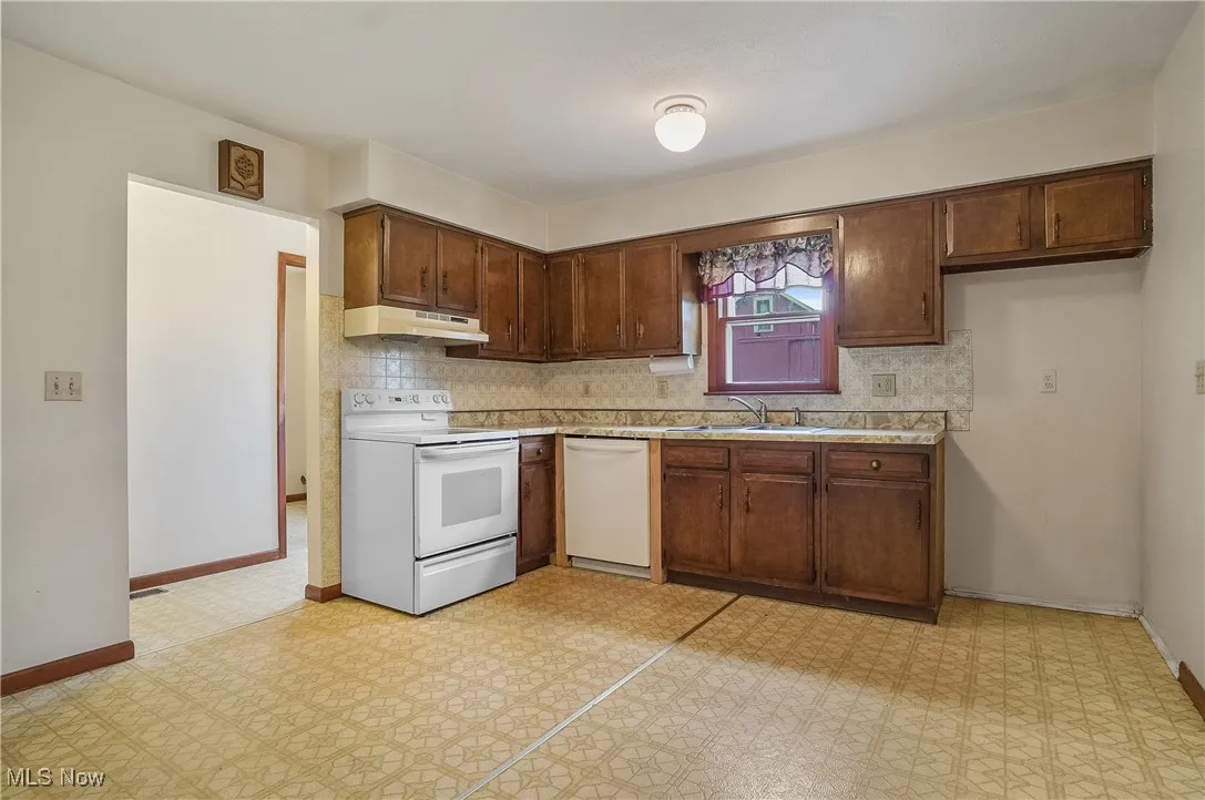 Kitchen featuring white appliances, under cabinet range hood, a sink, light countertops, and decorative backsplash