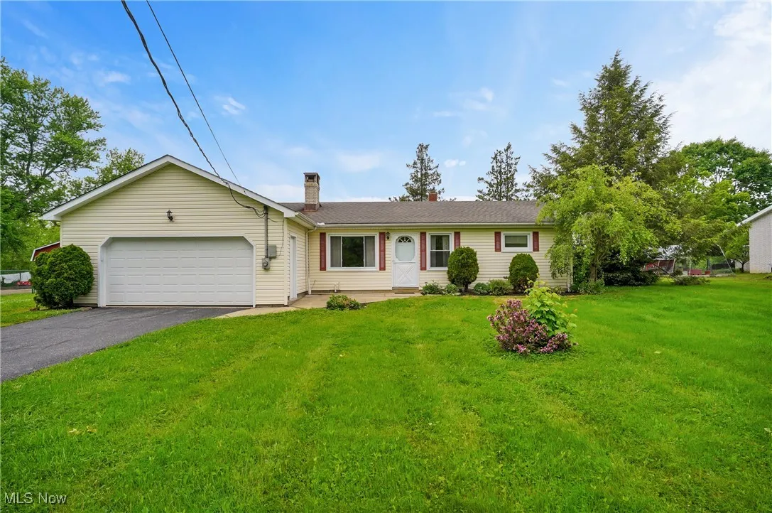 Single story home featuring asphalt driveway, an attached garage, a chimney, and a front lawn