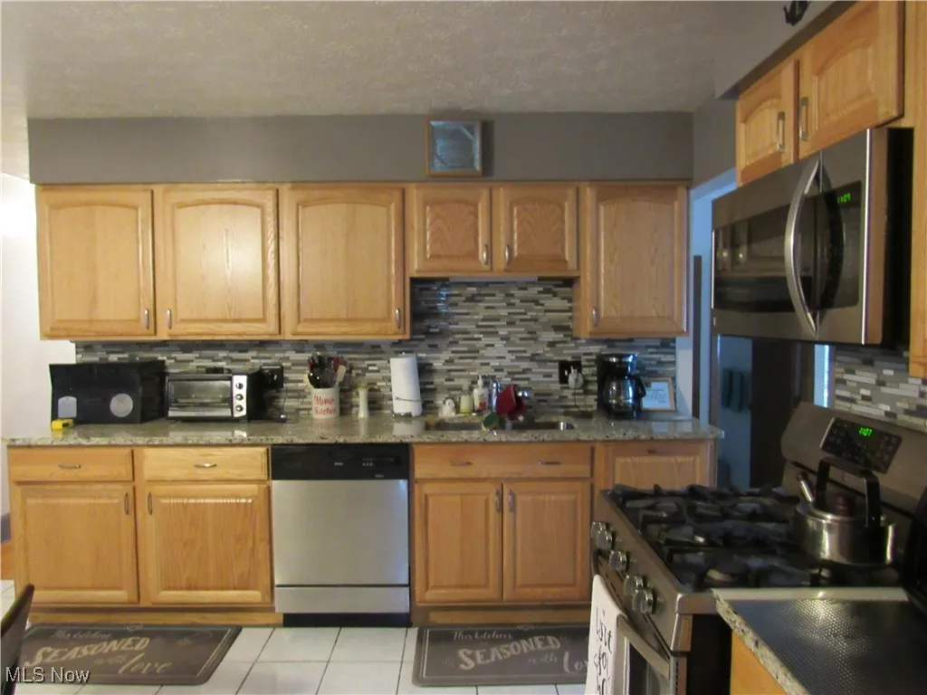 Kitchen with appliances with stainless steel finishes, backsplash, light tile patterned flooring, a sink, and a textured ceiling
