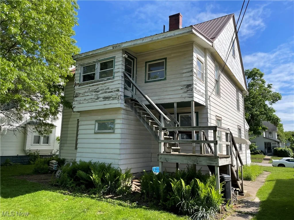 Rear view of property with a chimney, a lawn, and a deck