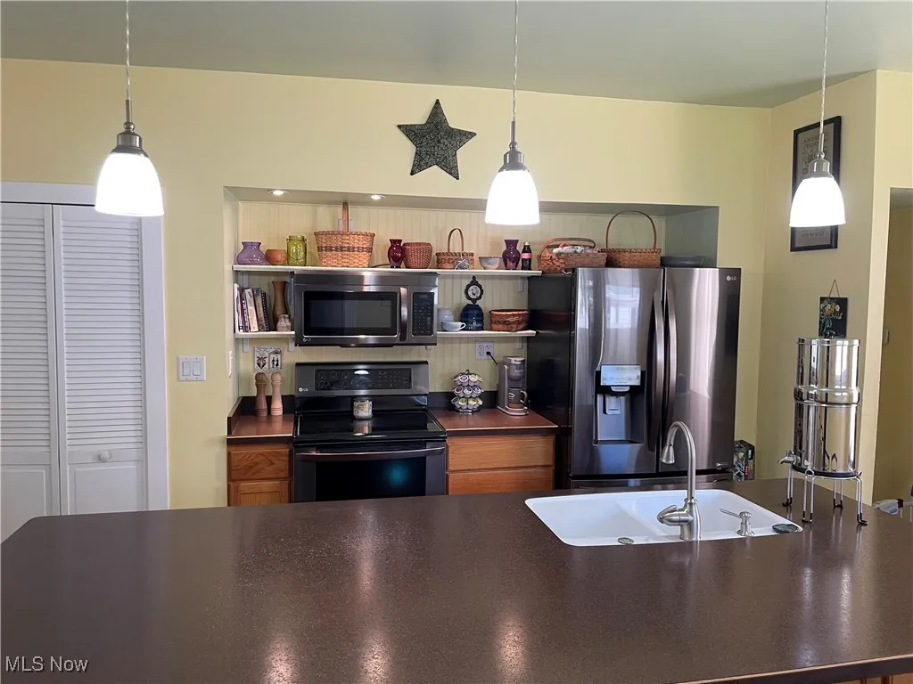 Kitchen featuring stainless steel appliances, dark countertops, a sink, and hanging light fixtures