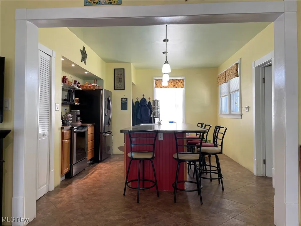 Kitchen with stainless steel appliances, a center island with sink, a breakfast bar, dark countertops, and pendant lighting