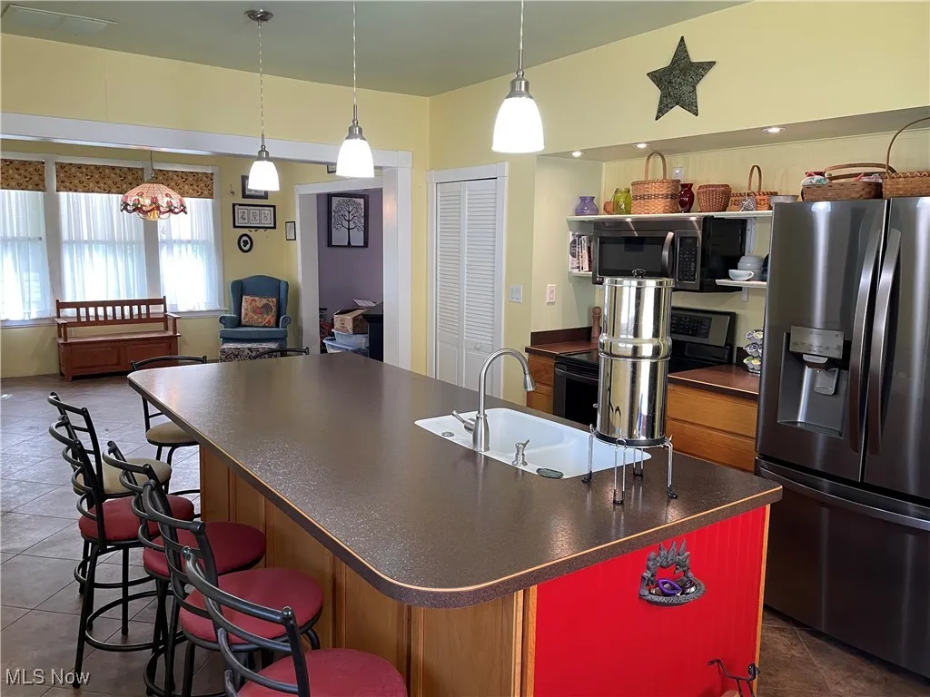 Kitchen featuring stainless steel appliances, a sink, dark countertops, an island with sink, and dark tile patterned floors