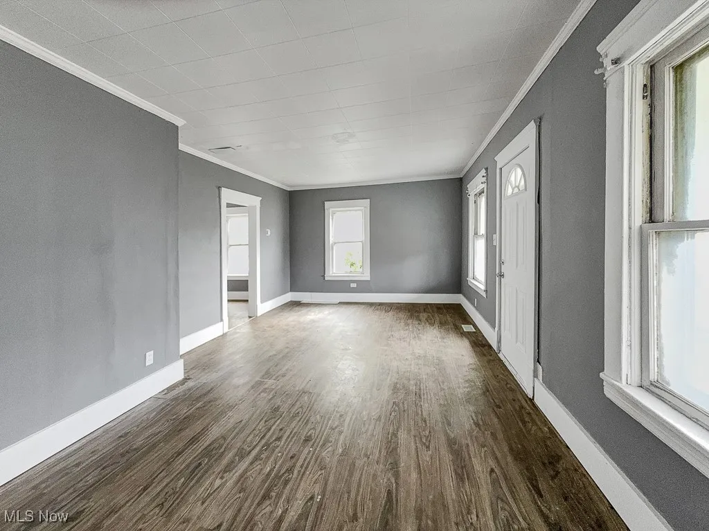 Empty room with crown molding, dark wood finished floors, and baseboards