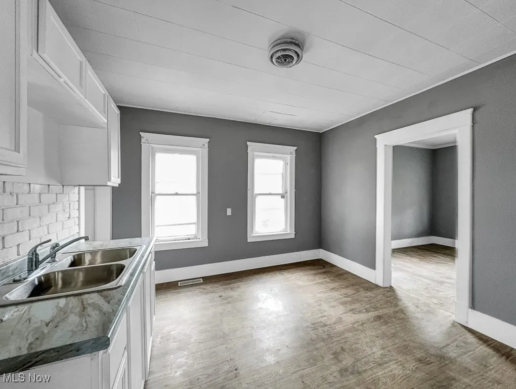 Kitchen featuring a sink, white cabinets, wood finished floors, decorative backsplash, and baseboards