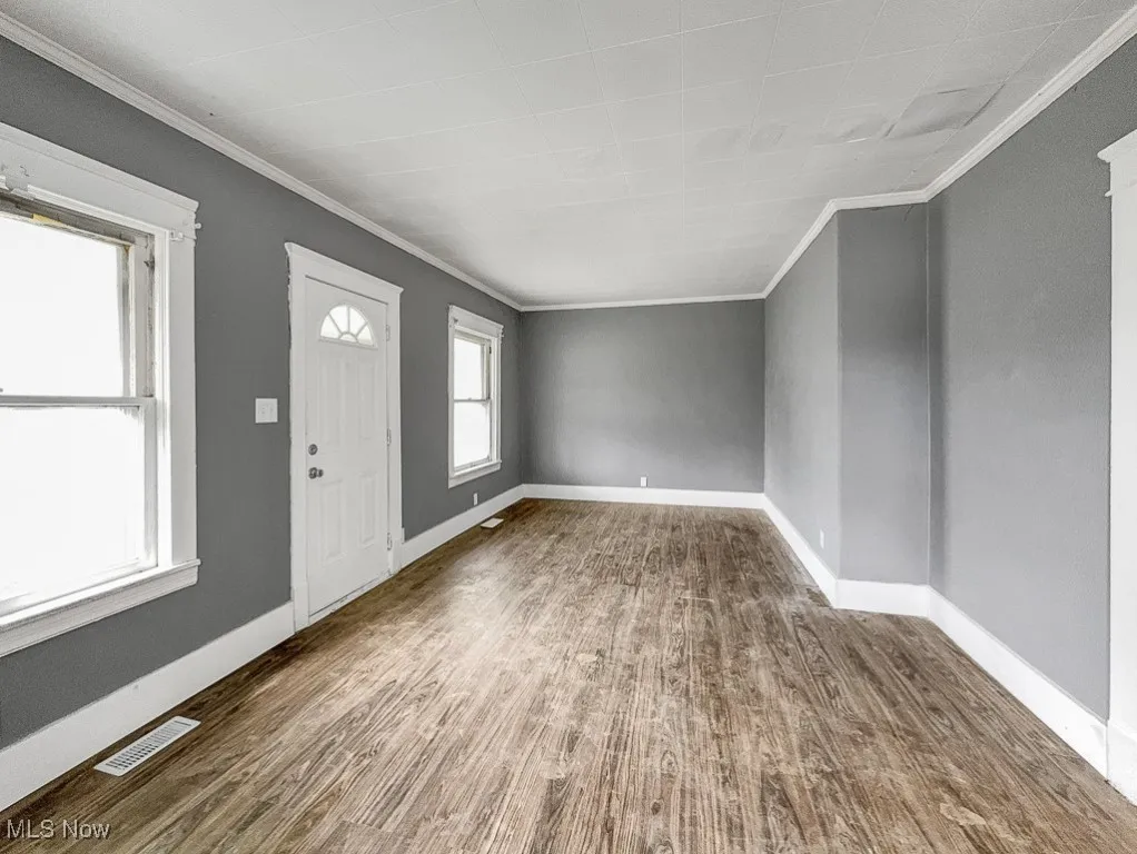 Entryway with ornamental molding, wood finished floors, and baseboards