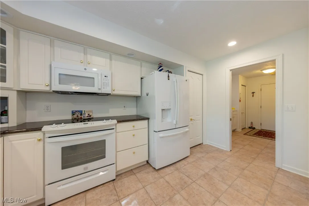 Kitchen with white appliances, dark countertops, white cabinets, and recessed lighting