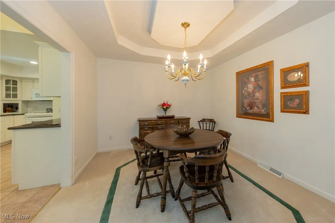 Dining area featuring a chandelier, a raised ceiling, baseboards, and light carpet