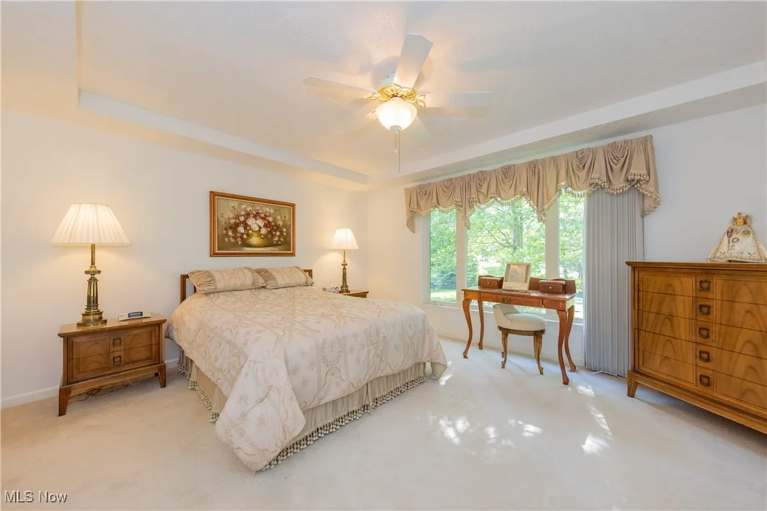 Bedroom featuring light colored carpet, a tray ceiling, baseboards, and a ceiling fan