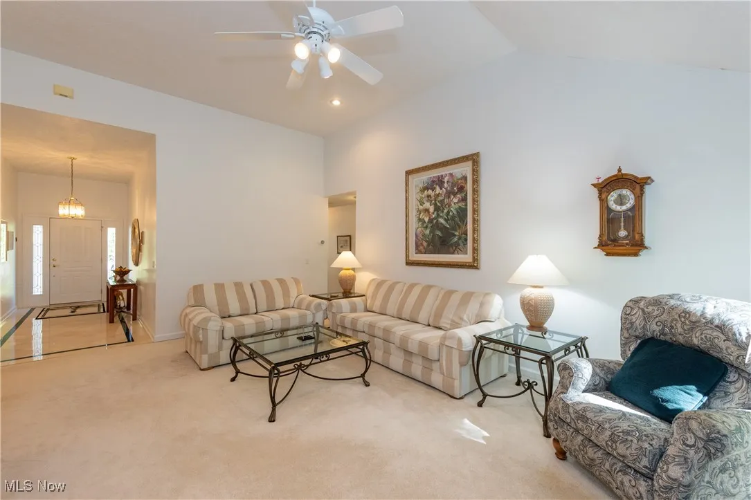 Living room featuring light colored carpet, ceiling fan, vaulted ceiling, and a chandelier