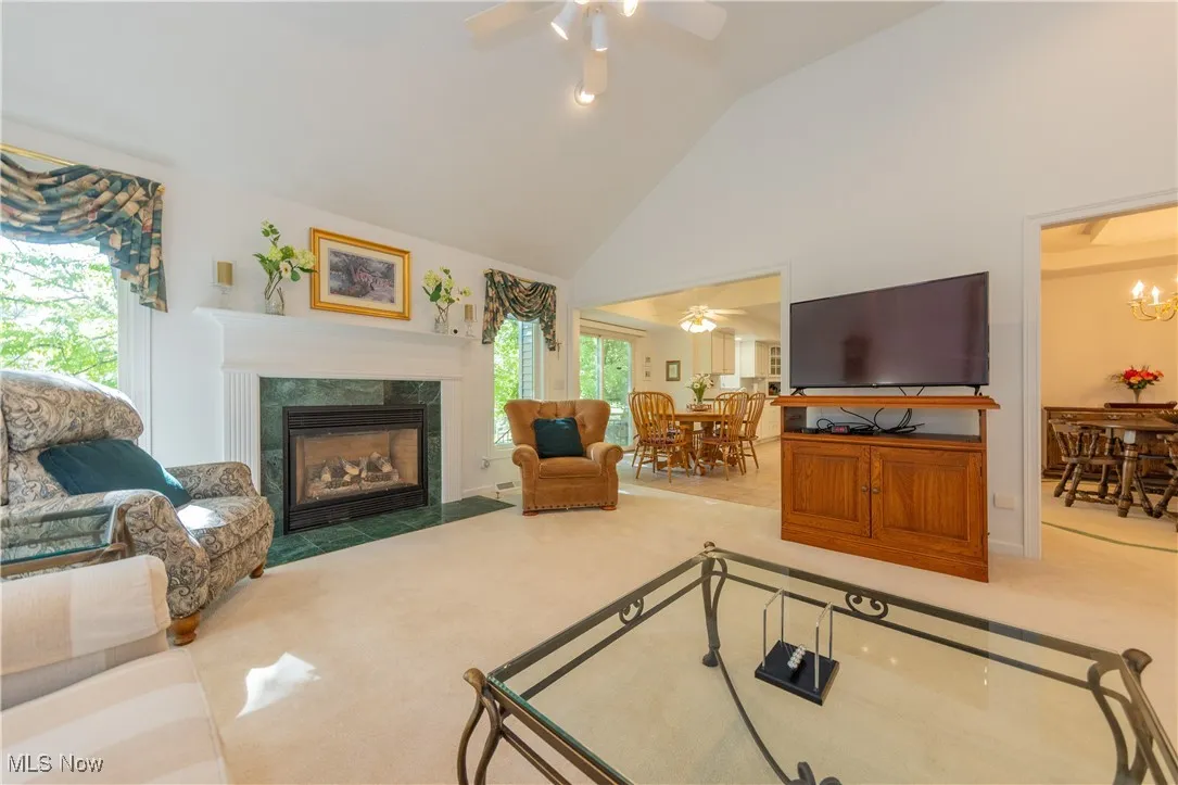 Carpeted living area with a ceiling fan, high vaulted ceiling, a high end fireplace, and a chandelier