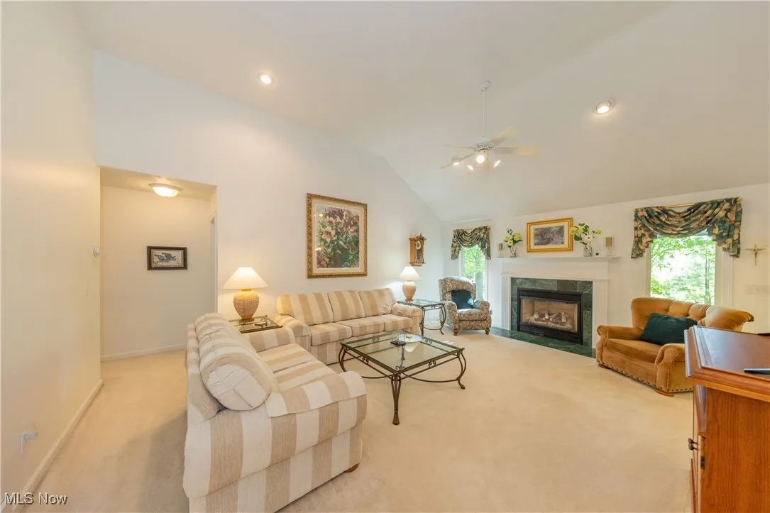 Living area with light colored carpet, ceiling fan, a fireplace, lofted ceiling, and baseboards