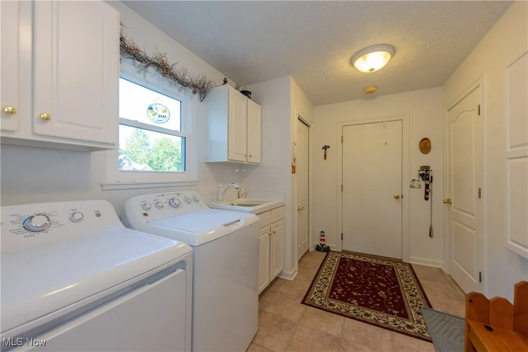 Laundry area with independent washer and dryer, cabinet space, light tile patterned flooring, and a textured ceiling