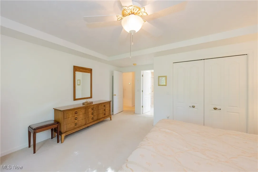Unfurnished bedroom with light colored carpet, a closet, baseboards, ceiling fan, and a raised ceiling