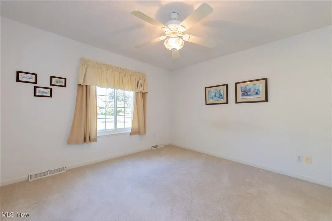 Spare room with light colored carpet, baseboards, and ceiling fan
