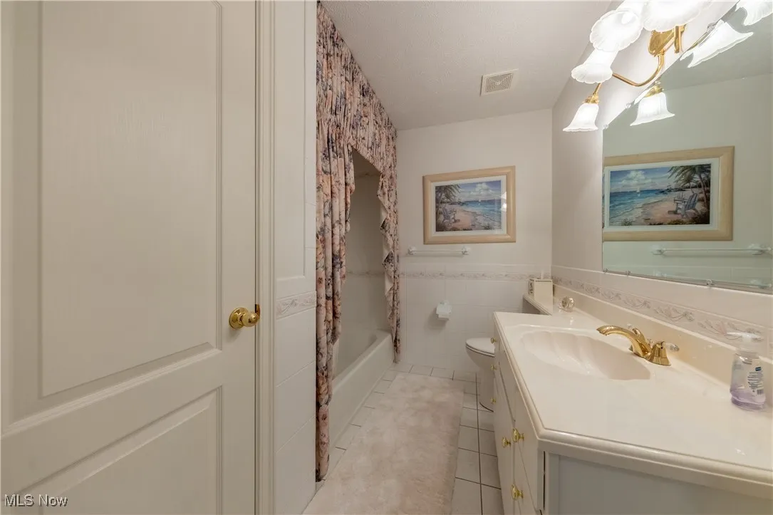 Full bath featuring tile patterned flooring, toilet, vanity, tile walls, and a wainscoted wall