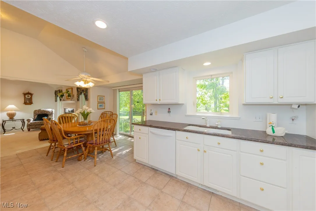 Kitchen featuring a sink, dishwasher, dark stone countertops, lofted ceiling, and white cabinetry