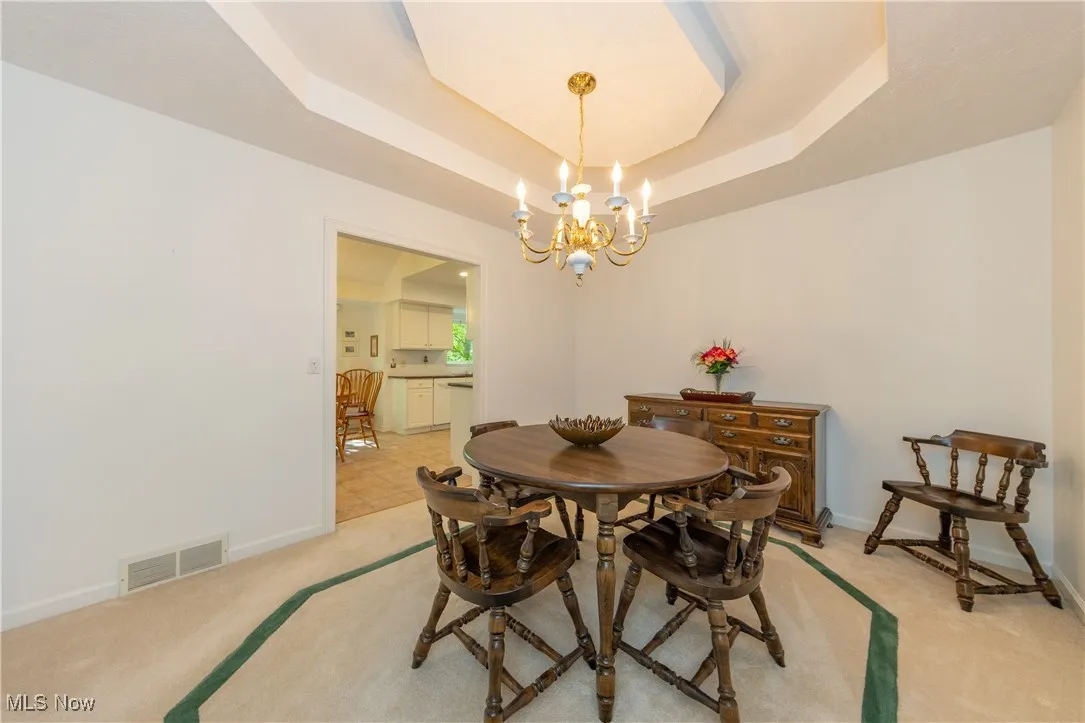 Dining area featuring light carpet, a chandelier, a tray ceiling, and baseboards