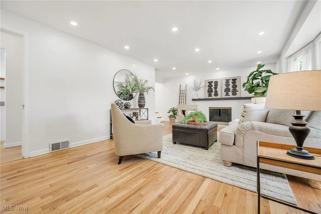 Living room with wood finished floors, recessed lighting, a brick fireplace, and baseboards