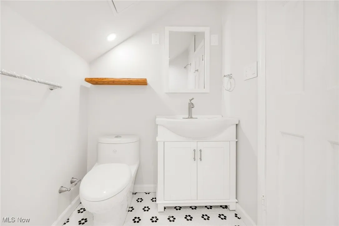 Half bath with baseboards, toilet, vanity, and lofted ceiling