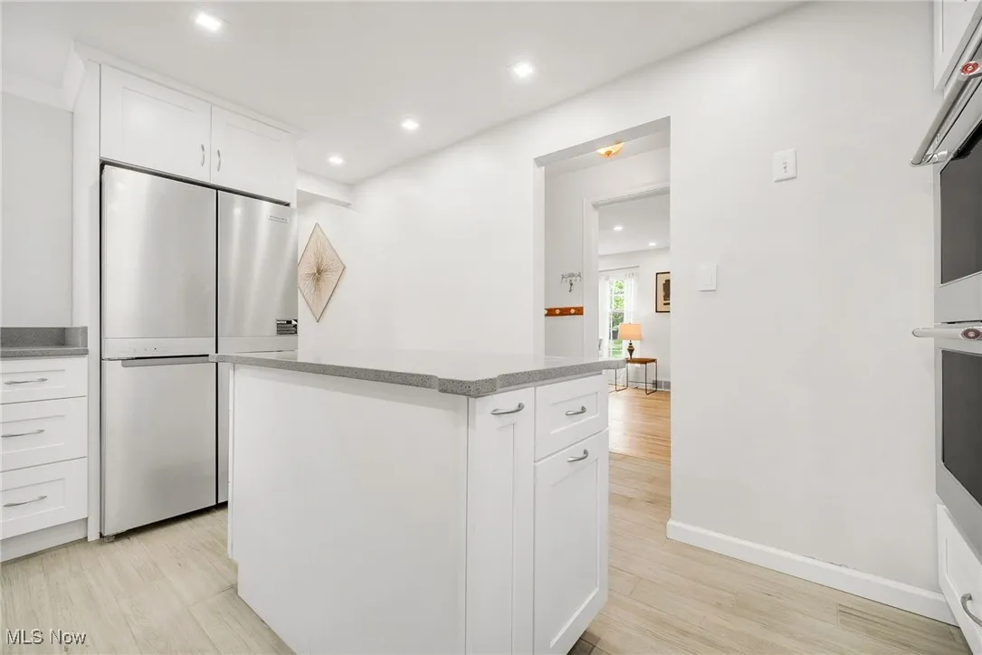 Kitchen with appliances with stainless steel finishes, a center island, recessed lighting, white cabinets, and light wood-type flooring
