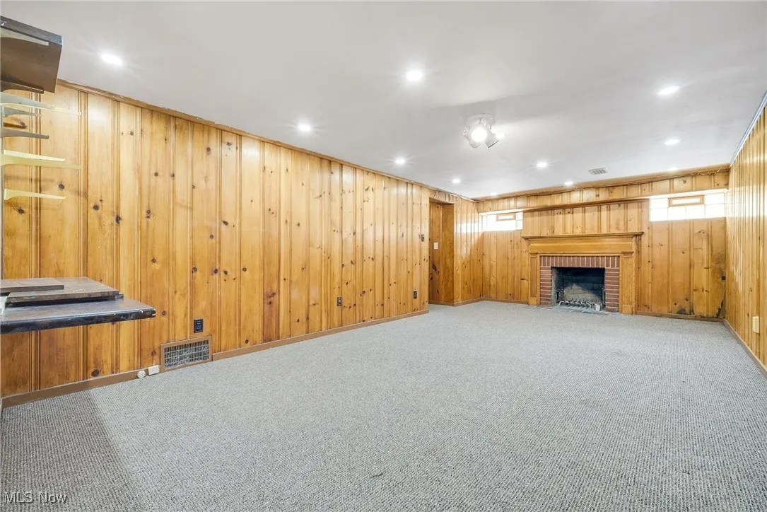 Unfurnished living room featuring a fireplace, wooden walls, recessed lighting, carpet, and healthy amount of natural light
