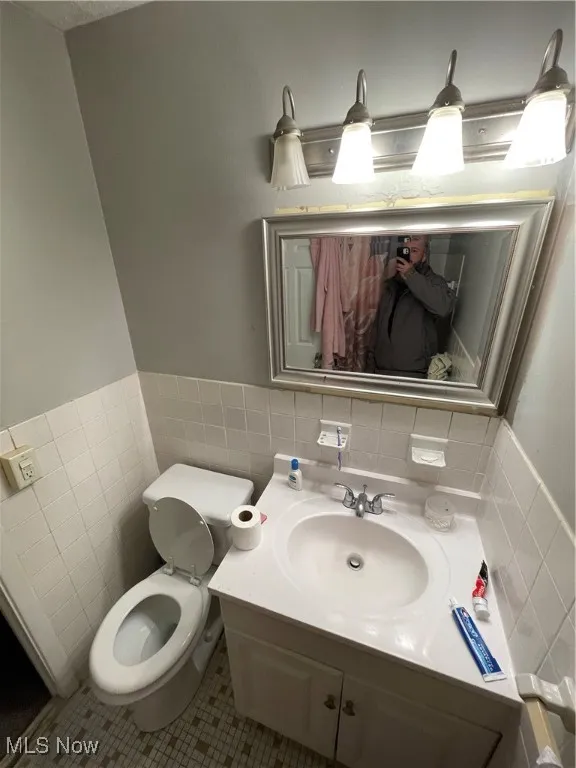 Half bath featuring tile walls, tile patterned floors, toilet, vanity, and a wainscoted wall