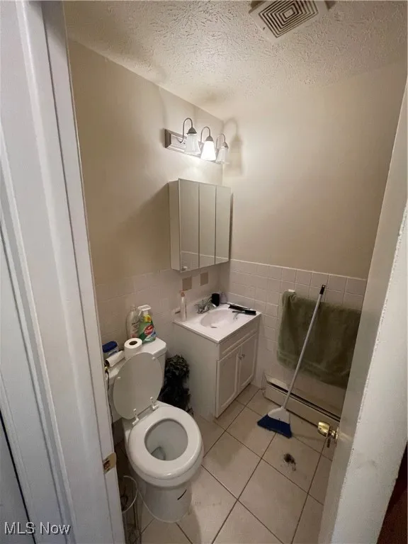 Bathroom featuring tile walls, a baseboard radiator, tile patterned floors, toilet, and wainscoting