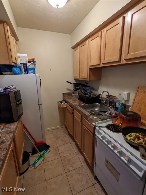 Kitchen with white electric range, a sink, light tile patterned flooring, dark countertops, and a textured ceiling