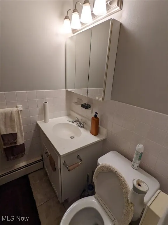 Bathroom with tile walls, a baseboard heating unit, vanity, toilet, and tile patterned flooring