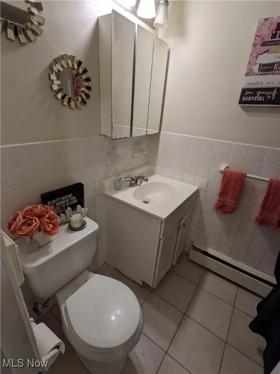Bathroom featuring tile walls, a baseboard heating unit, tile patterned flooring, toilet, and vanity