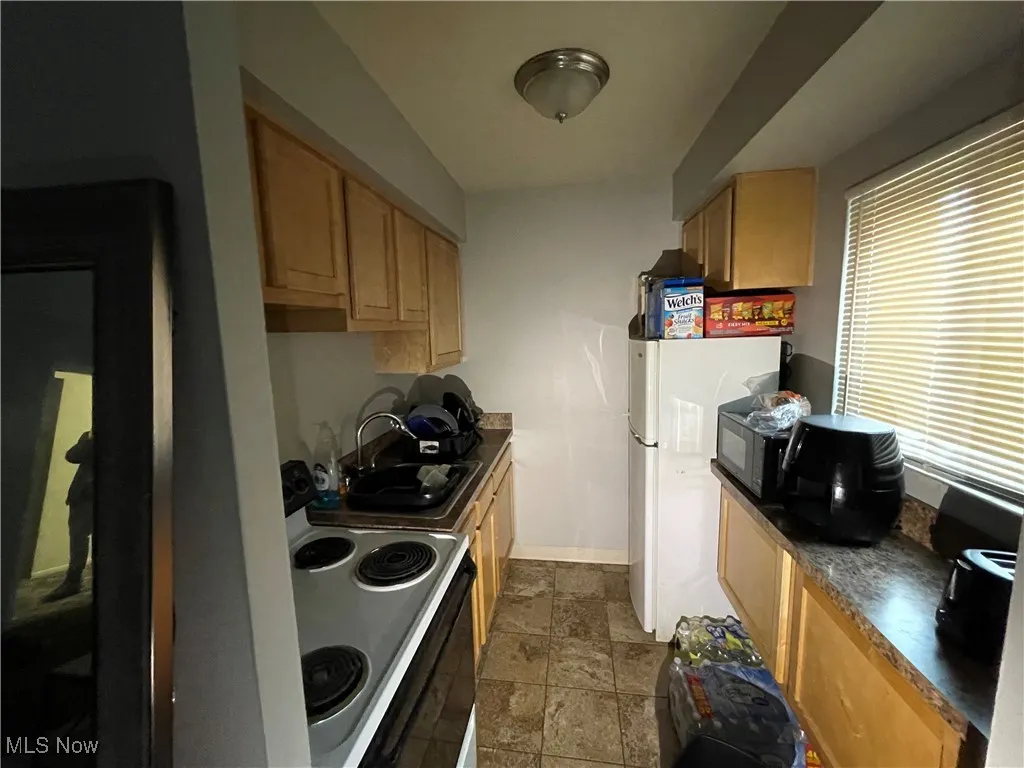 Kitchen featuring electric stove, a sink, stone tile flooring, dark countertops, and baseboards