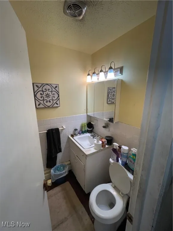 Half bath with tile walls, wainscoting, toilet, vanity, and a textured ceiling