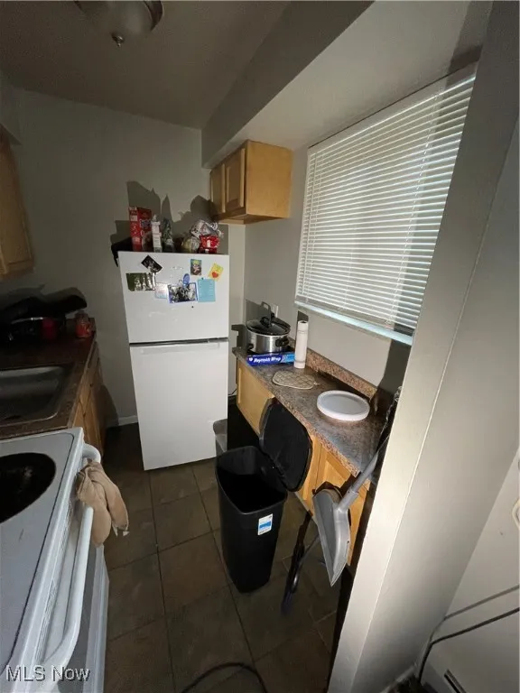 Kitchen featuring fridge, stove, a sink, dark tile patterned flooring, and light brown cabinetry