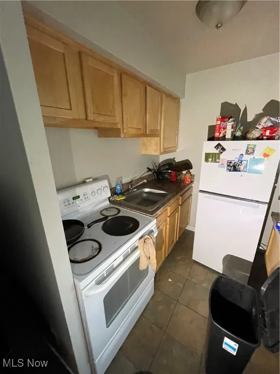 Kitchen featuring stove, fridge, a sink, dark tile patterned flooring, and light brown cabinetry