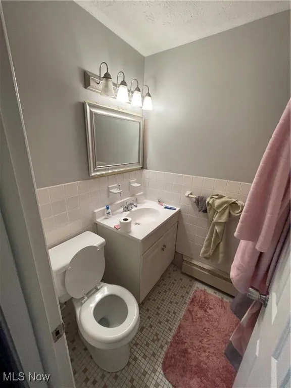 Bathroom with tile walls, a textured ceiling, toilet, a wainscoted wall, and tile patterned flooring