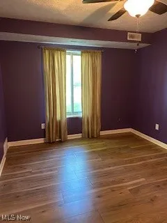 Spare room with a ceiling fan, baseboards, wood finished floors, and a textured ceiling