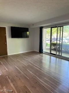 Empty room with a textured ceiling, baseboards, and hardwood / wood-style floors