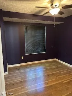 Empty room with baseboards, ceiling fan, wood finished floors, and a textured ceiling