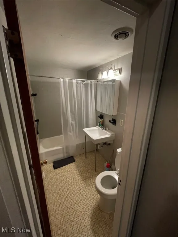 Bathroom featuring toilet, shower / tub combo, and a sink