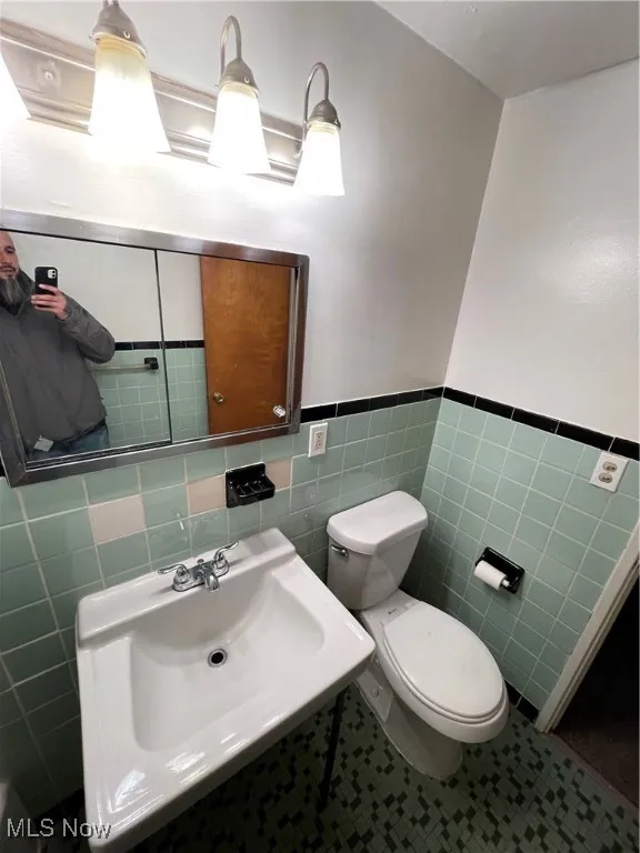 Bathroom with tile walls, a sink, toilet, and wainscoting